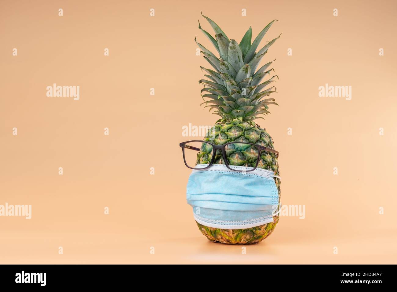 Interpretazione della frutta di ananas in forma umana durante una pandemia con occhiali e una maschera di protezione medico. Spazio di copia Foto Stock