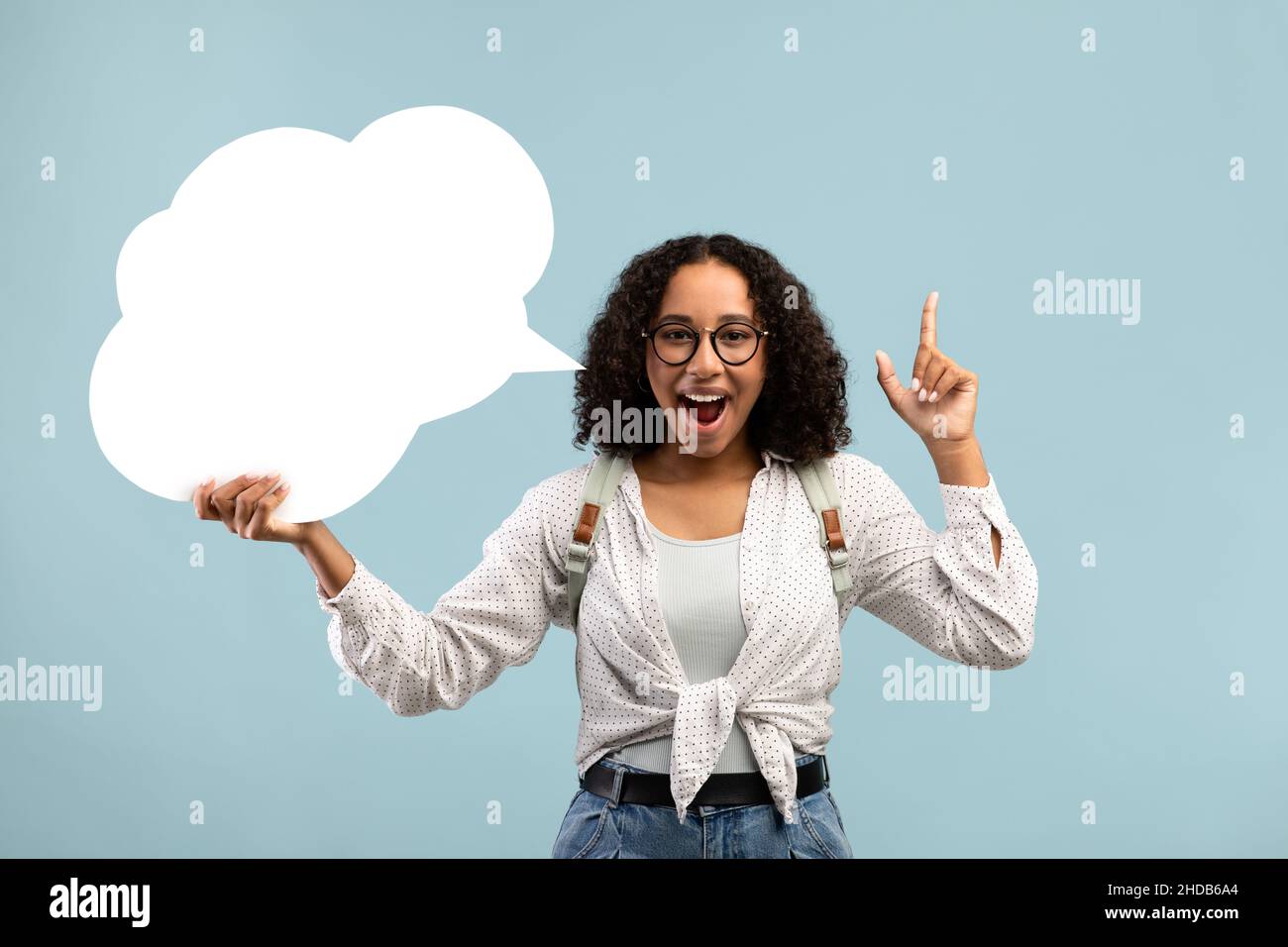 Felice donna nera che tiene vuoto bolla di parola, avendo idea creativa su sfondo blu studio, mockup per il design Foto Stock