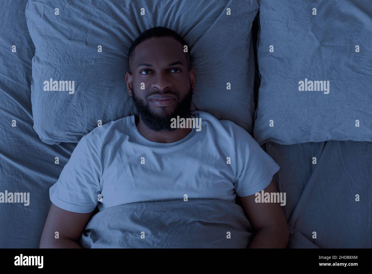 Uomo nero che si trova a letto e che pensa di notte Foto Stock