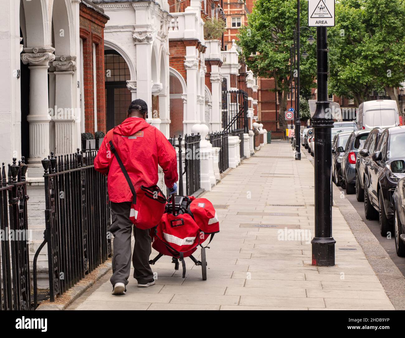 Un postino (recapito postale) che consegna posta/posta con un carrello a ruote lungo Harrington Gardens, Kensington, Londra Foto Stock