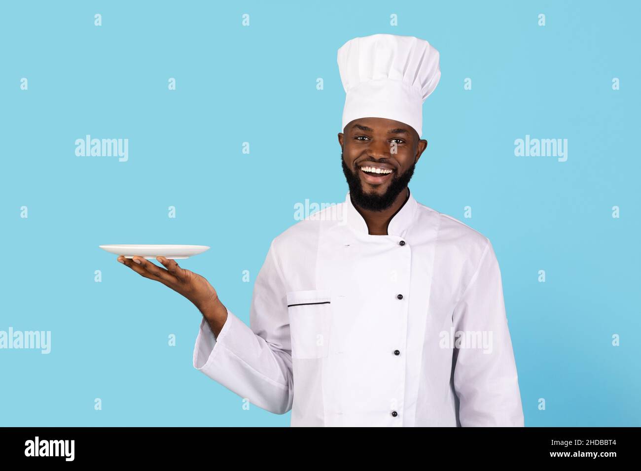 Ritratto di giovane giovane cuoco nero sorridente in uniforme che tiene piatto vuoto Foto Stock