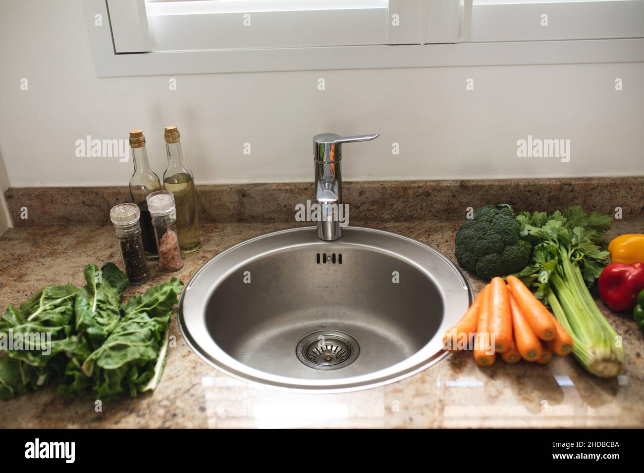 Varie verdure fresche crude e sane intorno al lavandino sul bancone della cucina a casa Foto Stock