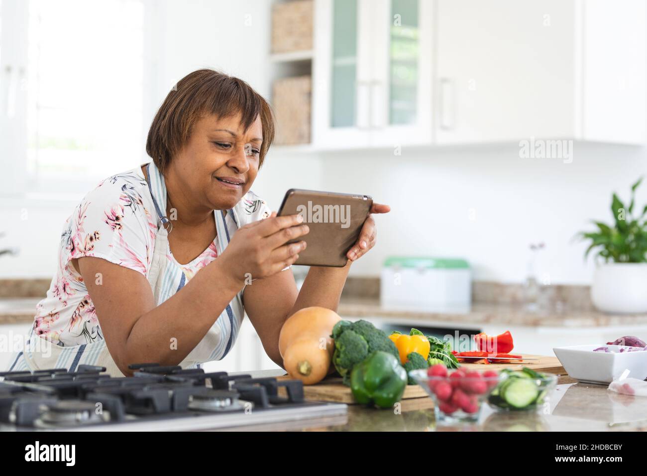Donna anziana che guarda la ricetta online sul tablet pc mentre cucinano cibo in cucina a casa Foto Stock