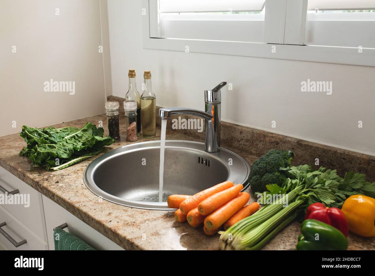 Varie verdure fresche crude sane sul banco da cucina mentre l'acqua corrente nel lavandino a casa Foto Stock