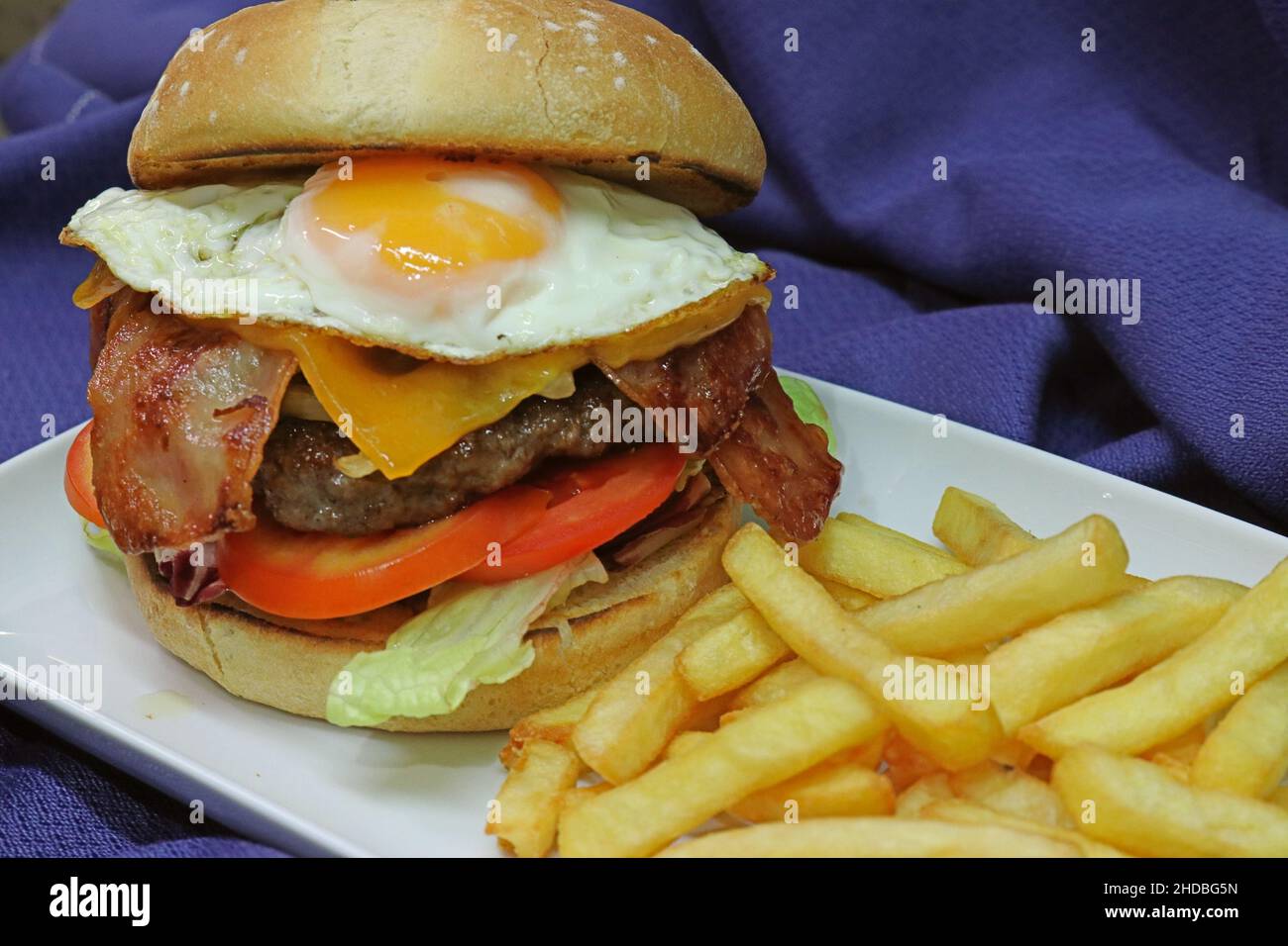 Foto di un panino con hamburger e pancetta con patatine fritte su un panno blu marino Foto Stock