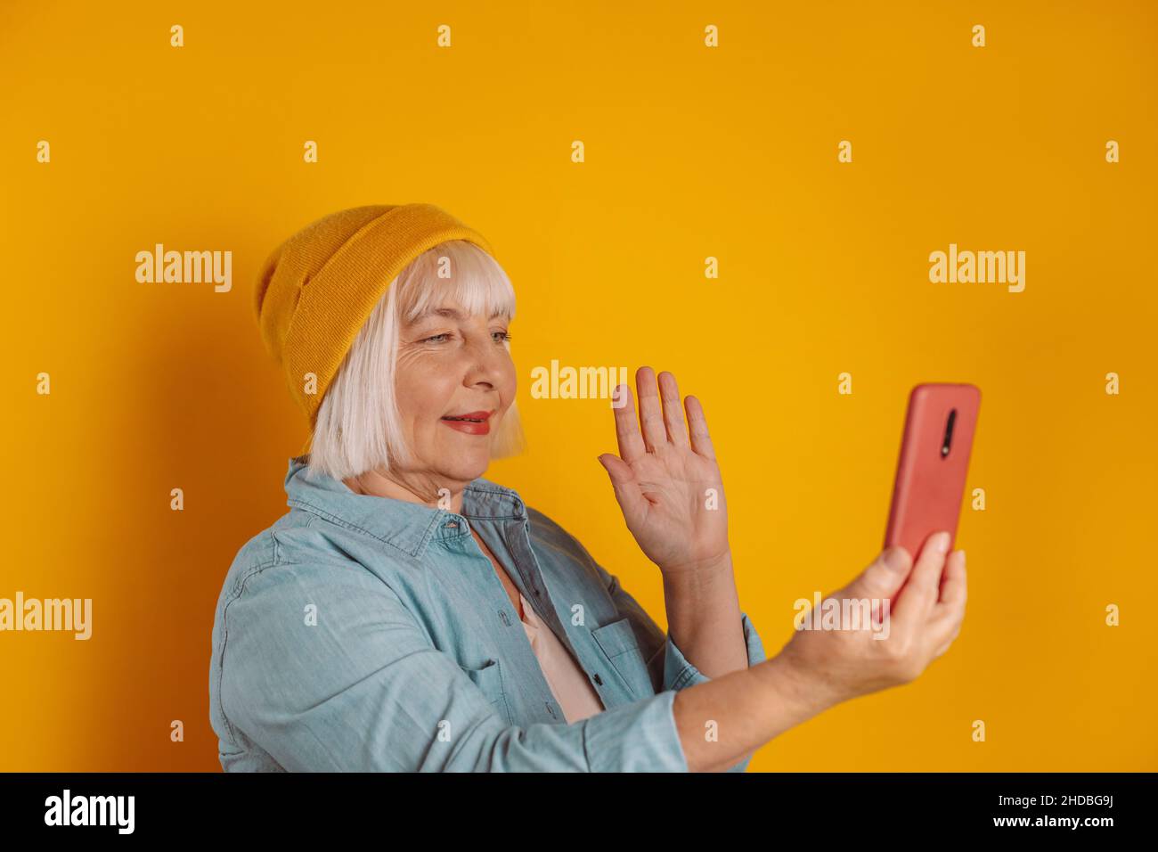 Ritratto di 50s allegro caucasico donna holning telefono, avendo online conferenza buon umore isolato su sfondo luminoso colore Foto Stock