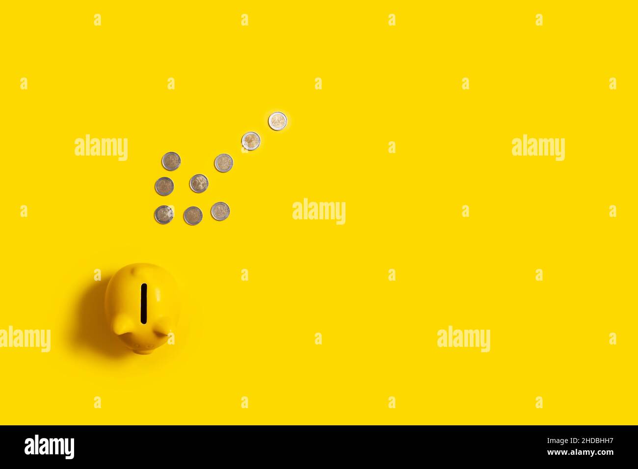freccia fatta con monete in euro che punta ad una banca piggy con fondo giallo con spazio pubblicitario Foto Stock