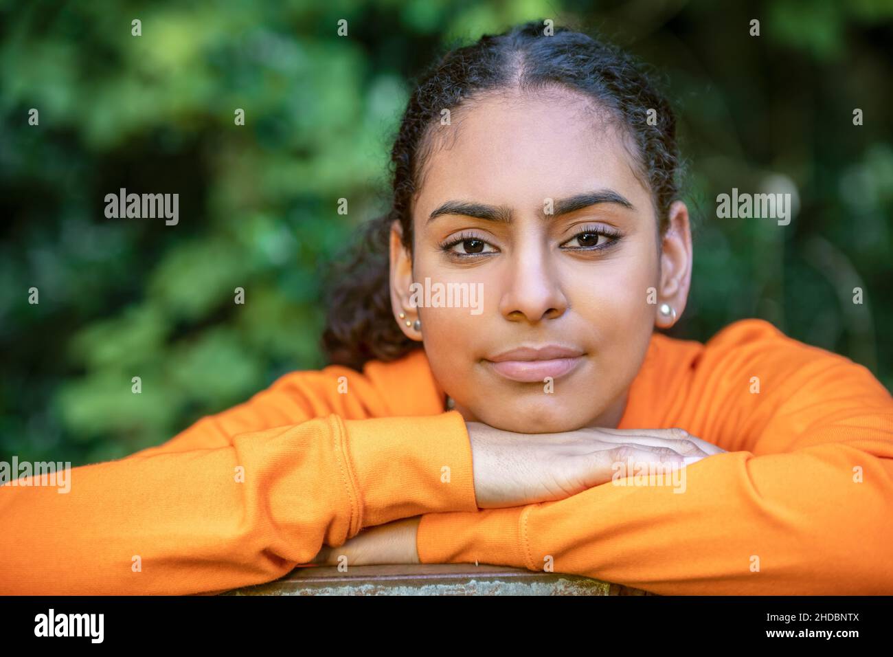 Ritratto all'aperto di bella felice gara mista African American ragazza adolescente femmina giovane donna che pensa e sorridendo con un naturale verde lascia indietro Foto Stock