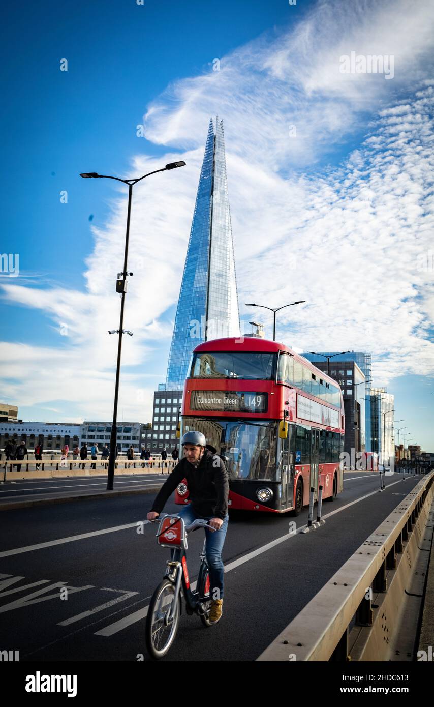 Un ciclista seguito da un autobus rosso di Londra attraversa il London Bridge in direzione nord con l'iconico edificio The Shard sullo sfondo. Foto Stock