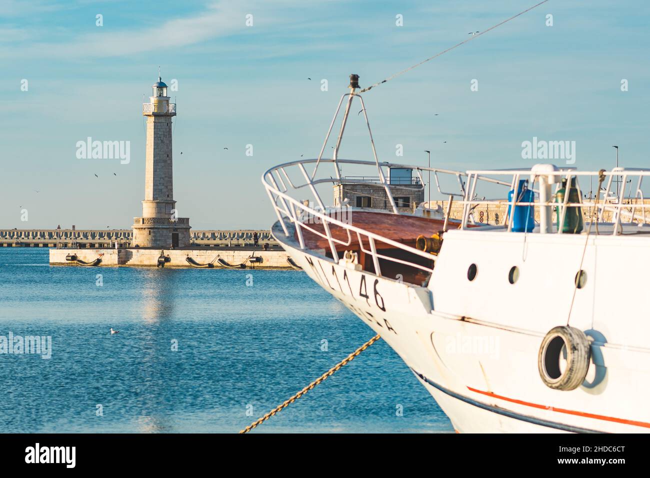 Prua di vecchia barca da pesca ancorata e bellissimo faro sullo sfondo con mare blu e calmo Foto Stock