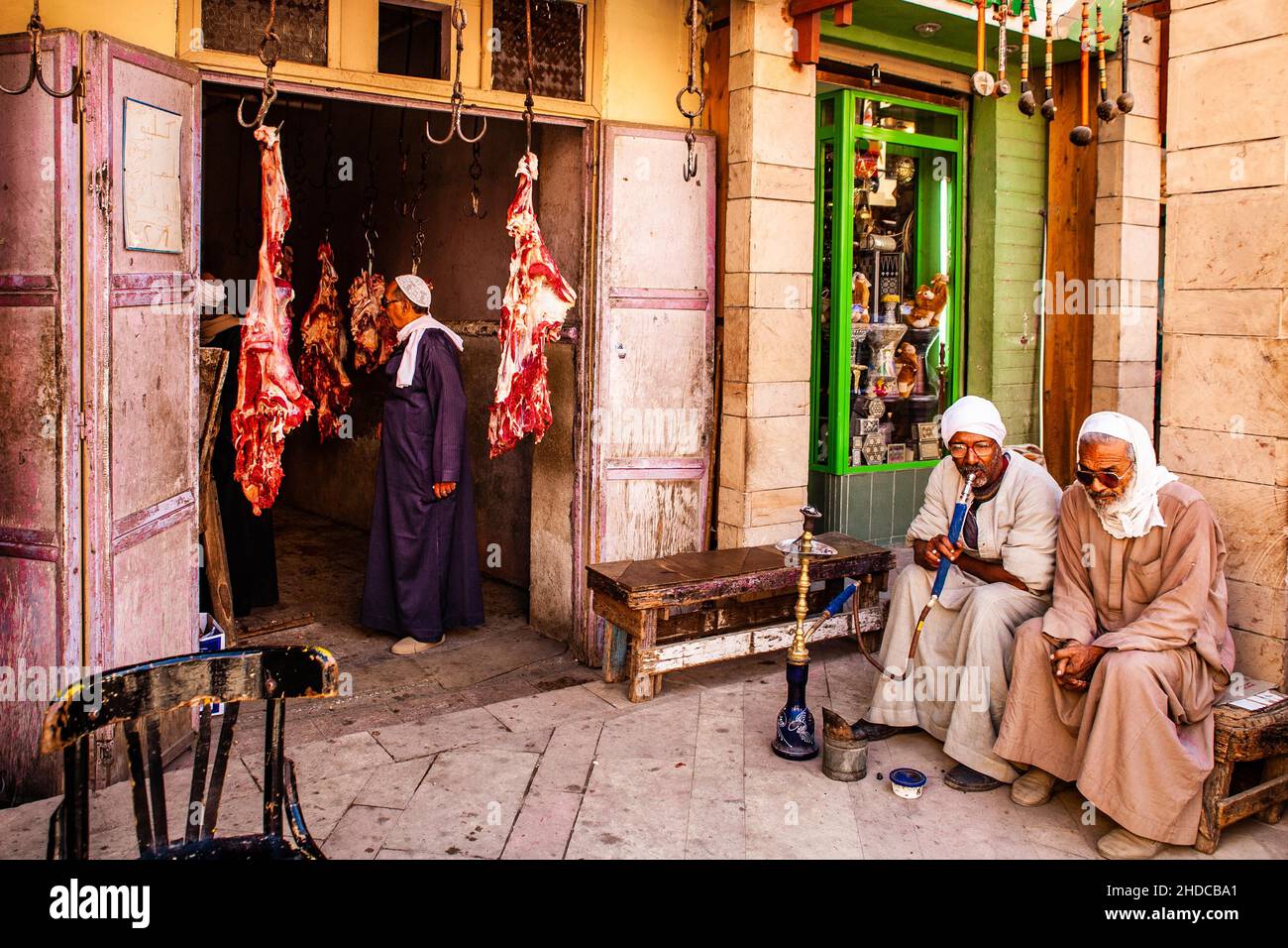 Uomini che fumano pipe d'acqua di fronte ad un macellaio, bazar nella Città Vecchia, Luxor, Tebe, Egitto, Luxor, Tebe, Egitto, Africa Foto Stock