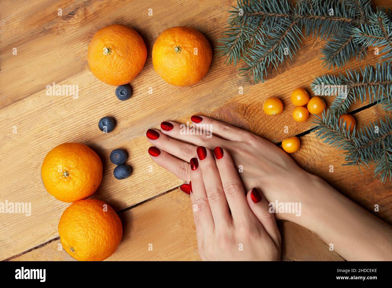 Le mani delle donne con manicure di borgogna che giacciono sul tavolo, vista dall'alto. Comfort domestico, tangerini, ramo di abete su sfondo legno. Foto di alta qualità Foto Stock