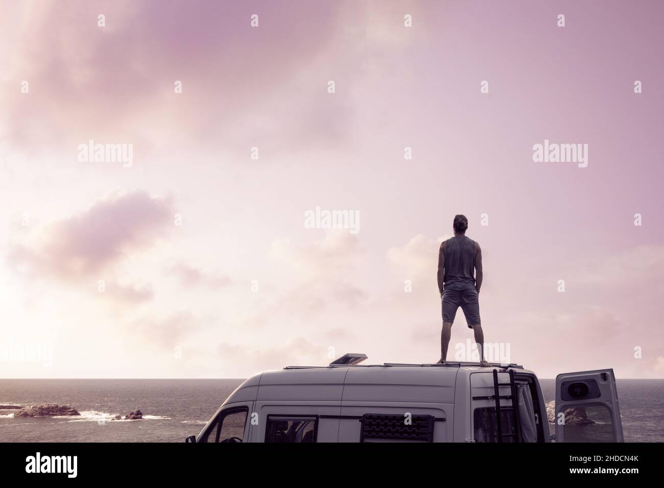 Uomo in piedi sulla cima di un camper vicino all'oceano Foto Stock
