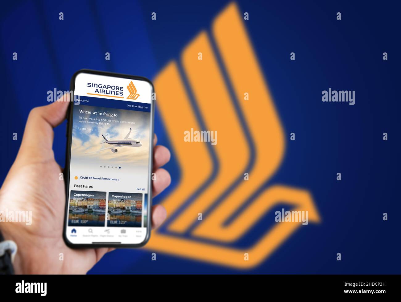 Singapore, ottobre 2021: Tenere a mano un telefono con la richiesta di prenotazione dei voli Singapore Airlines. Logo Singapore Airlines sfocato su sfondo blu Foto Stock