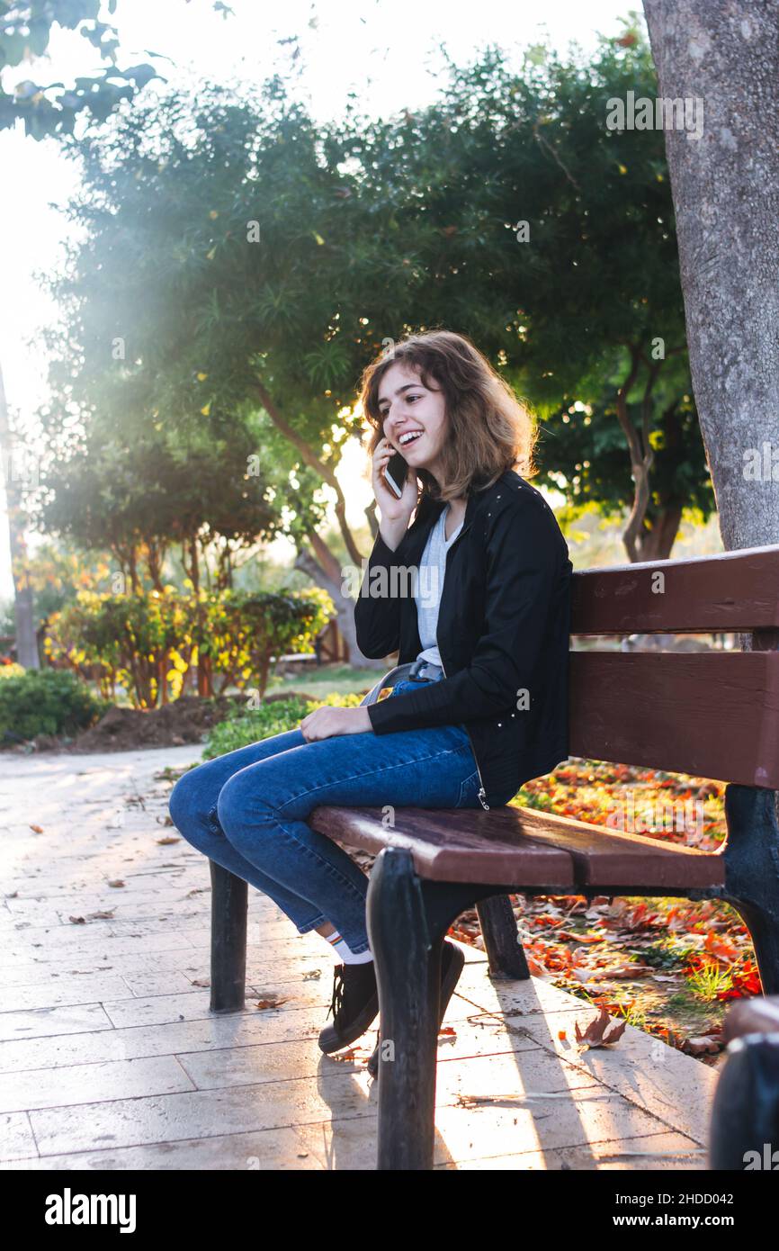Ragazza adolescente che prende per telefono sulla panca nel parco Foto Stock