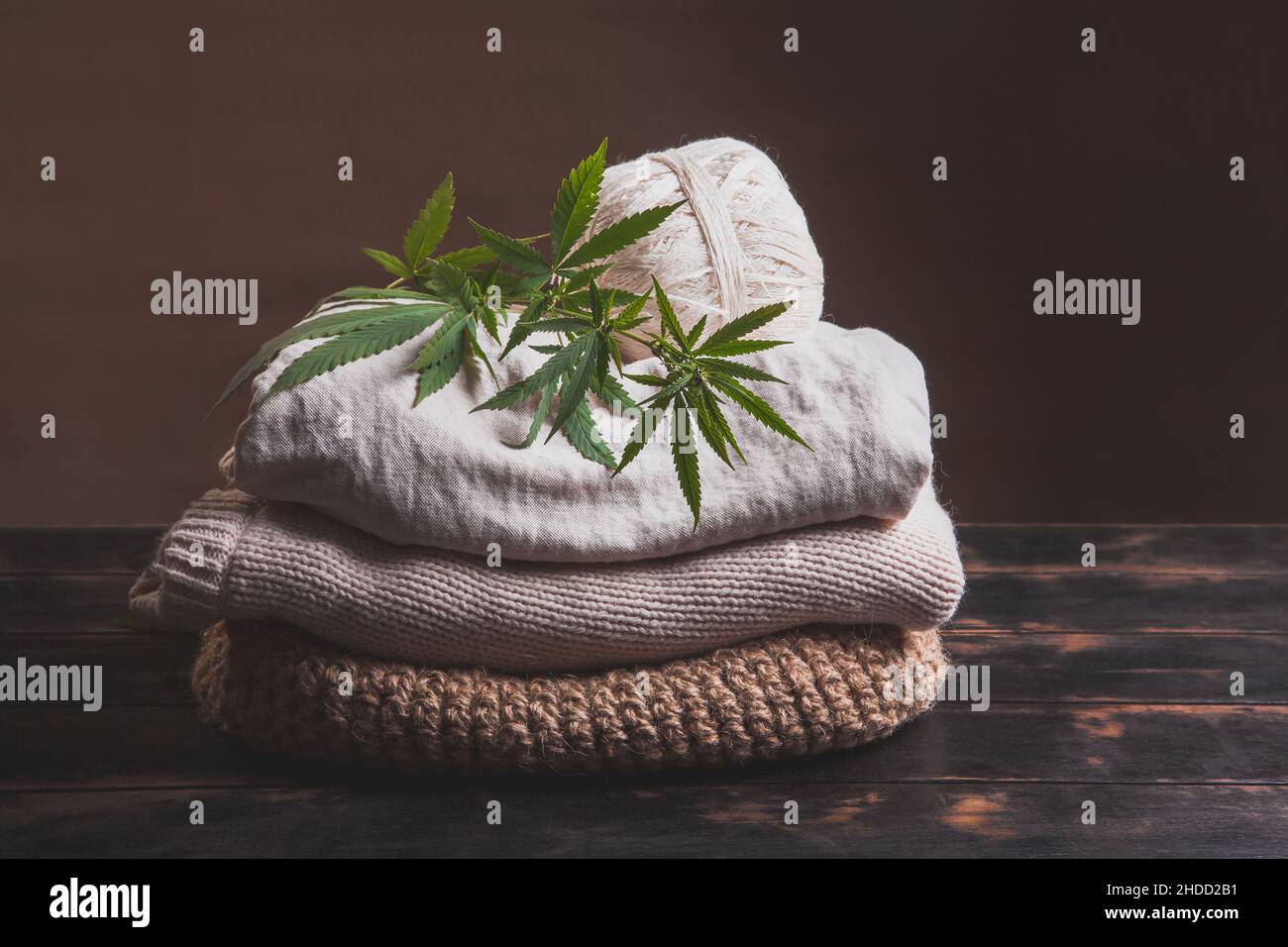 Una pila di vari tipi di tessuti di fibre di canapa. Fili di canapa, filati e tessuti con foglie di cannabis su sfondo ligneo. Foto Stock