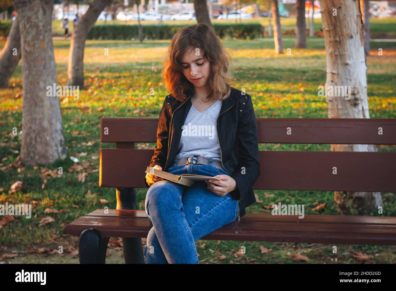 Ragazza allegra che legge libro su panchina al parco autunnale Foto Stock