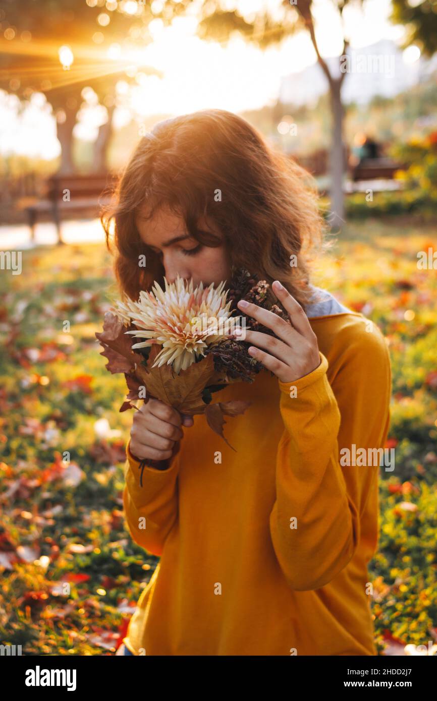 Giovane ragazza curly in maglione giallo sull'erba con bouquet autunnale di foglie secche e fiori Foto Stock