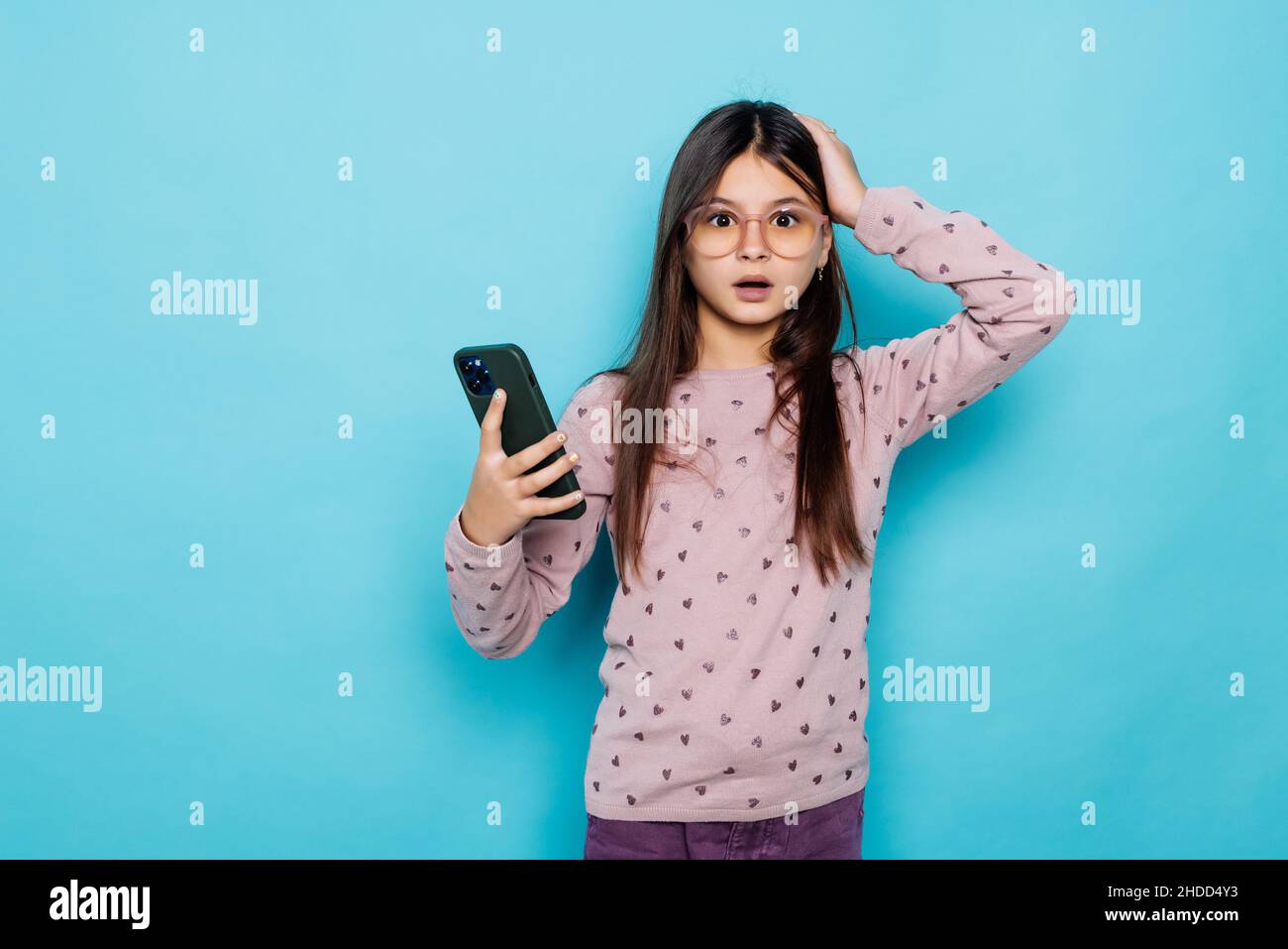 Caucasian kid girl contro il muro blu tenere mano tecnologia moderna utilizzare touch viso palma stupito urlo impressionato Wow omg incredibile inaspettato Foto Stock