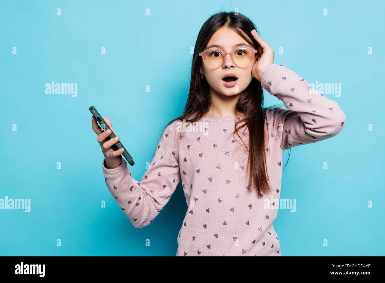 Caucasian kid girl contro il muro blu tenere mano tecnologia moderna utilizzare touch viso palma stupito urlo impressionato Wow omg incredibile inaspettato Foto Stock
