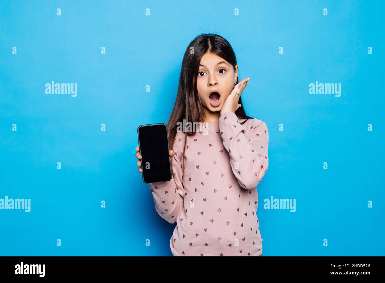 Ragazza bionda caucasica che indossa la T-shirt rosa contro il muro blu tenere mano tecnologia moderna utilizzare il tocco Foto Stock