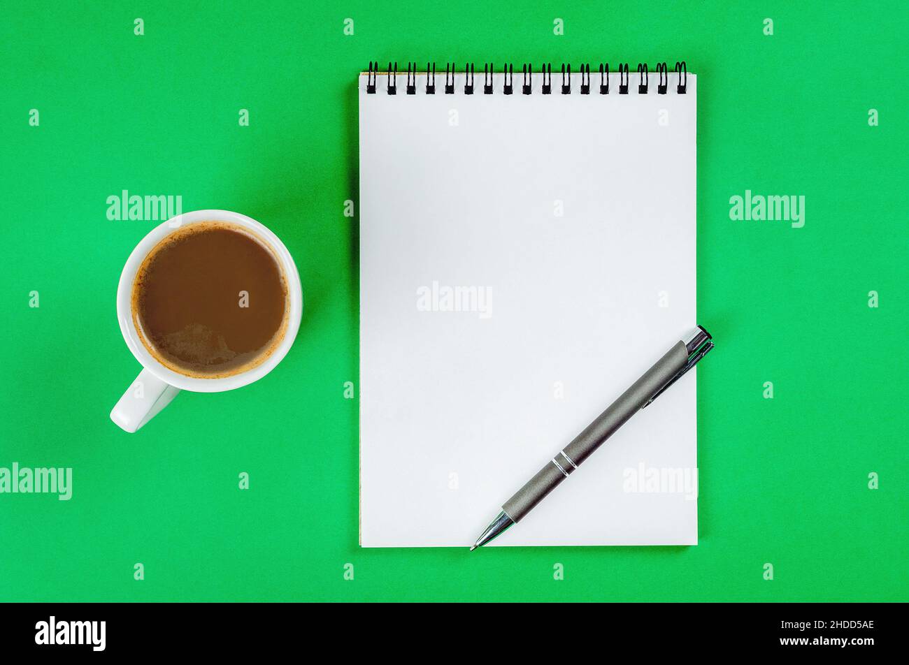 Blocco note con pagine bianche, penna e tazza di caffè su sfondo verde chiaro. Foto Stock