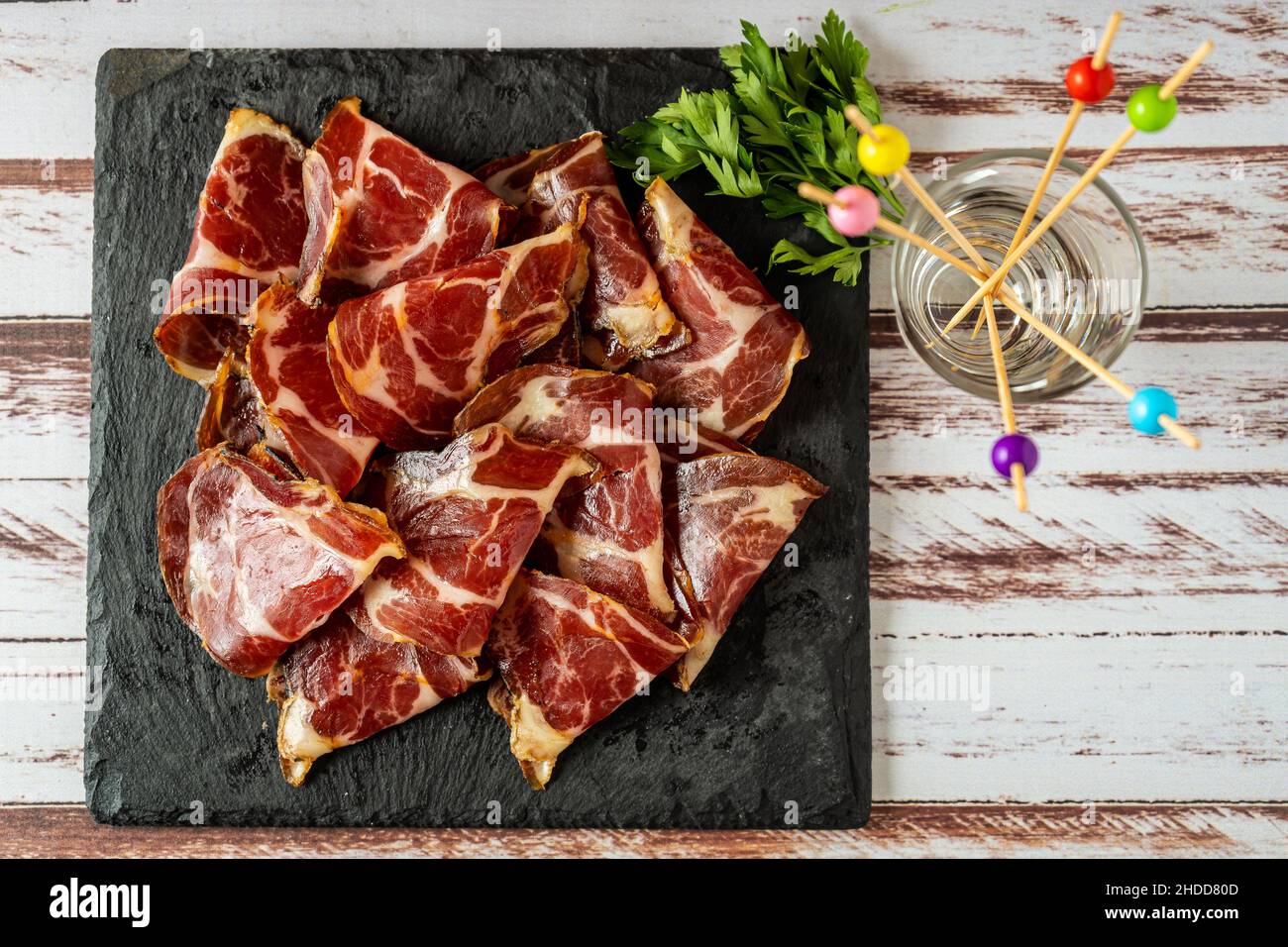 Vista dall'alto di alcune squisite fetas de bondiola o maiale crudo sottaceto su una lastra nera su un tavolo rustico. Foto Stock