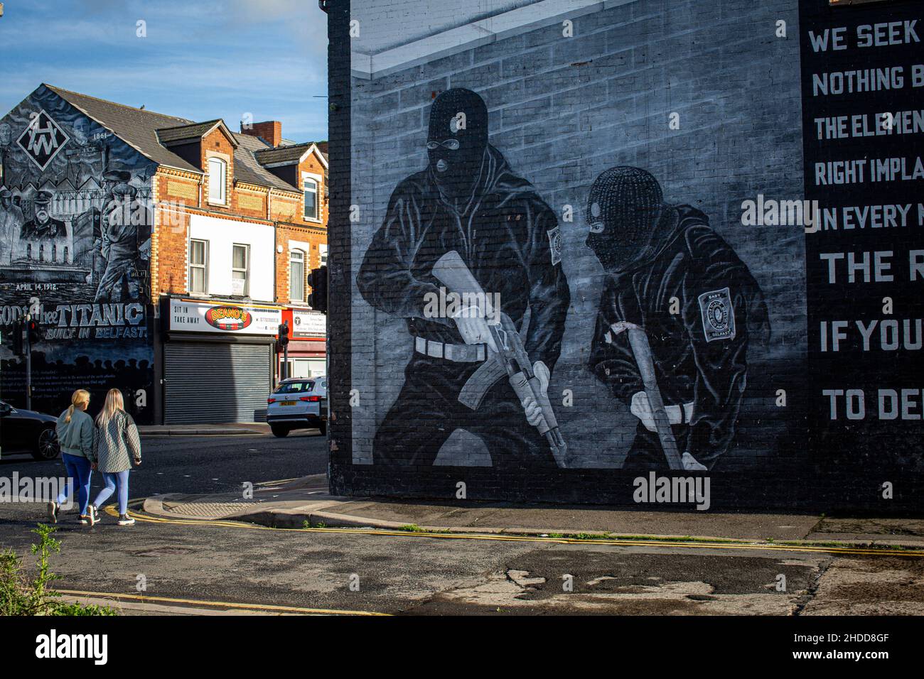 Due giovani donne che passano davanti a un murale paramilitare lealista sulla strada Newtownards il 8th novembre 2021 a Belfast, nell'Irlanda del Nord. Foto Stock