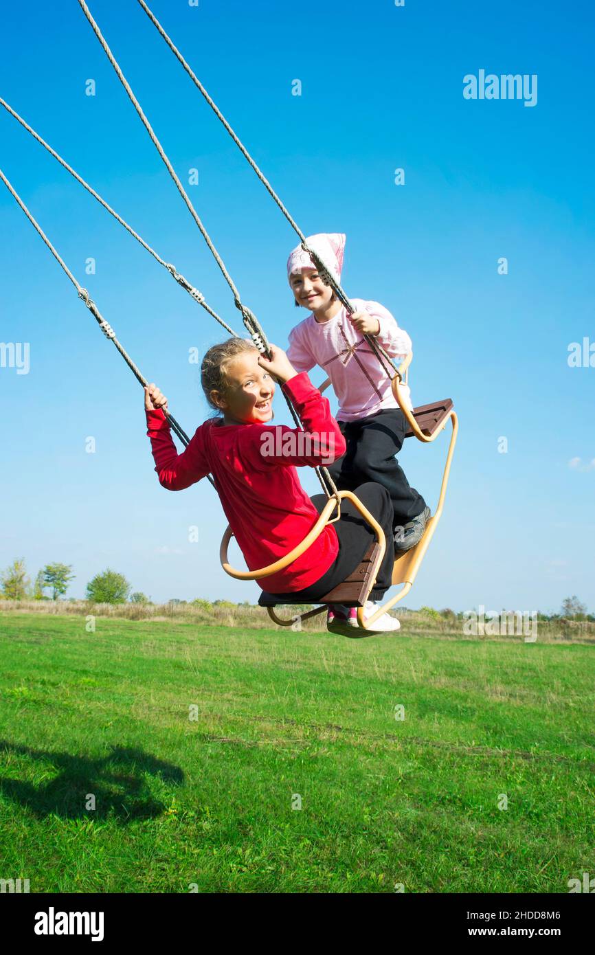 Due ragazze felici che si siedono sull'altalena divertendosi al parco giochi nel giorno d'estate soleggiato. Foto Stock