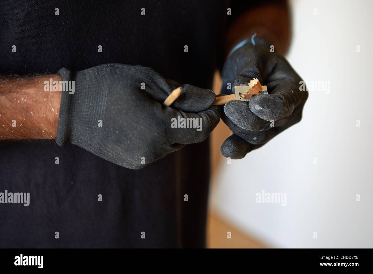 Primo piano delle mani di una persona con guanti affilando una matita Foto Stock