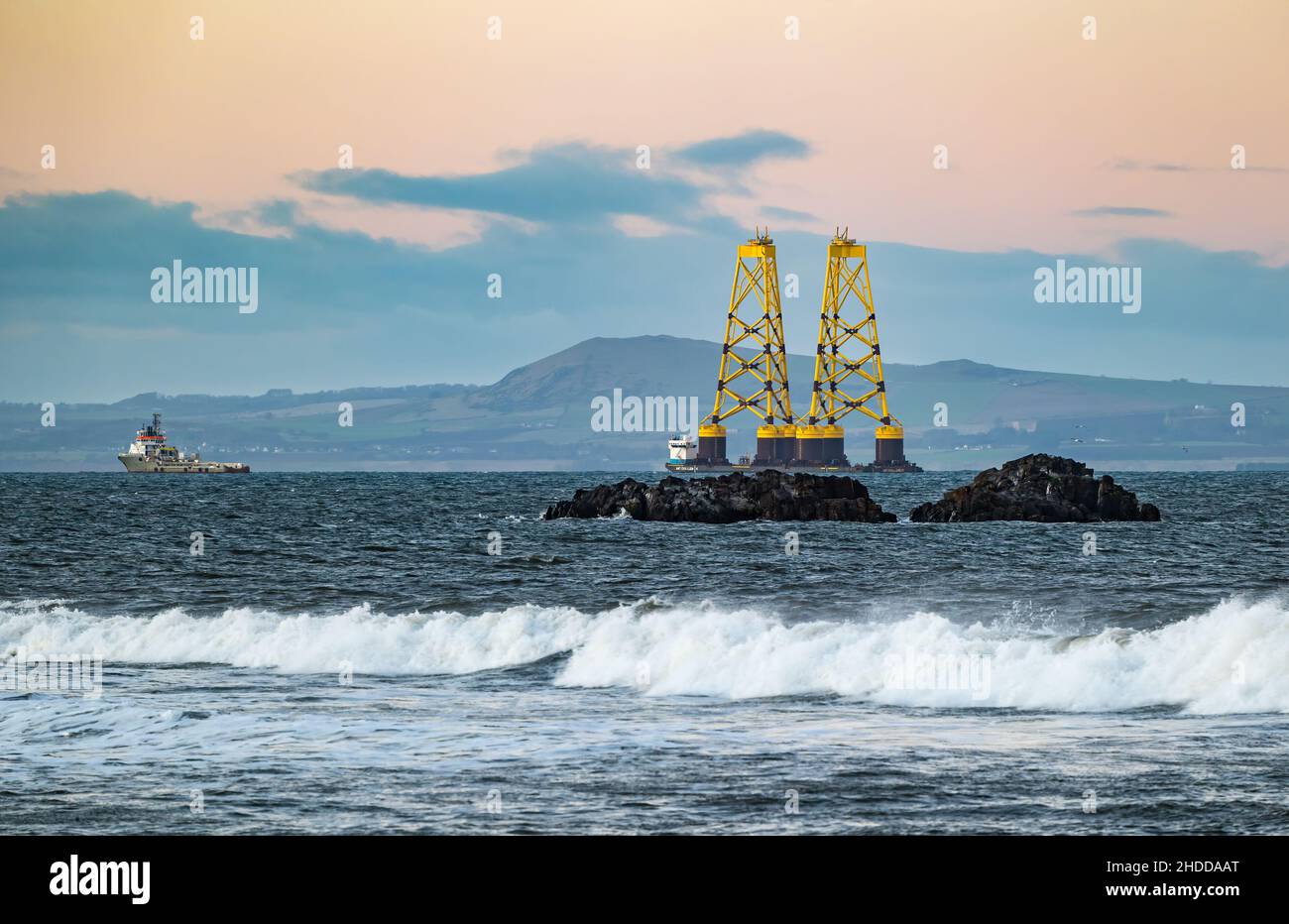 Al tramonto, Firth of Forth, Scozia, Regno Unito, una chiatta che trasporta due enormi turbine eoliche gialle si dirige verso il Mare del Nord Foto Stock