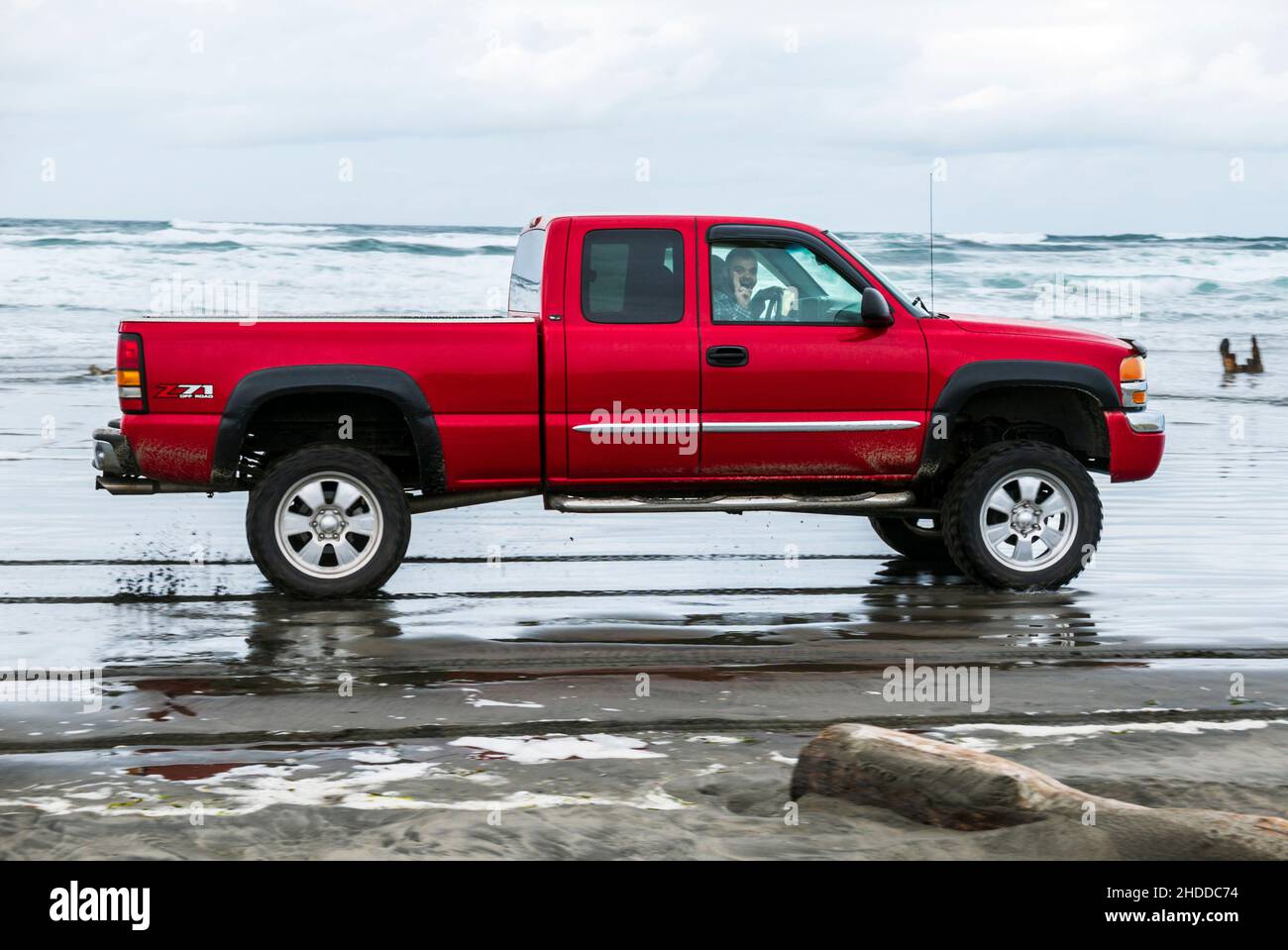 I turisti guidano il camion rosso attraverso le onde dell'oceano; Fort Stevens state Park; Hammond; Oregon; USA Foto Stock