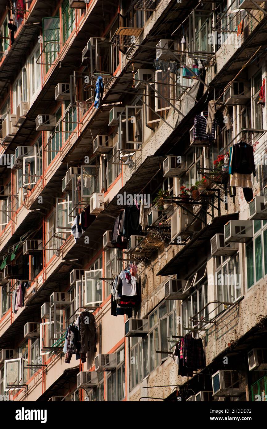 Condizionatori d'aria, fiori e lavanderia si trovano all'esterno di un edificio di appartamenti a più piani ad Hong Kong. Foto Stock