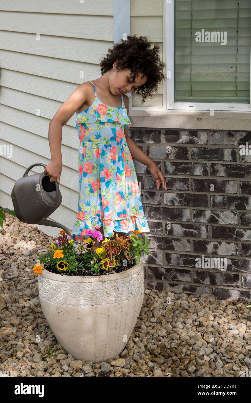 Vadnais Heights, Minnesota. Una bambina birazziale di sei anni in un bel vestito che innaffia i fiori con un annaffiatoio. Foto Stock