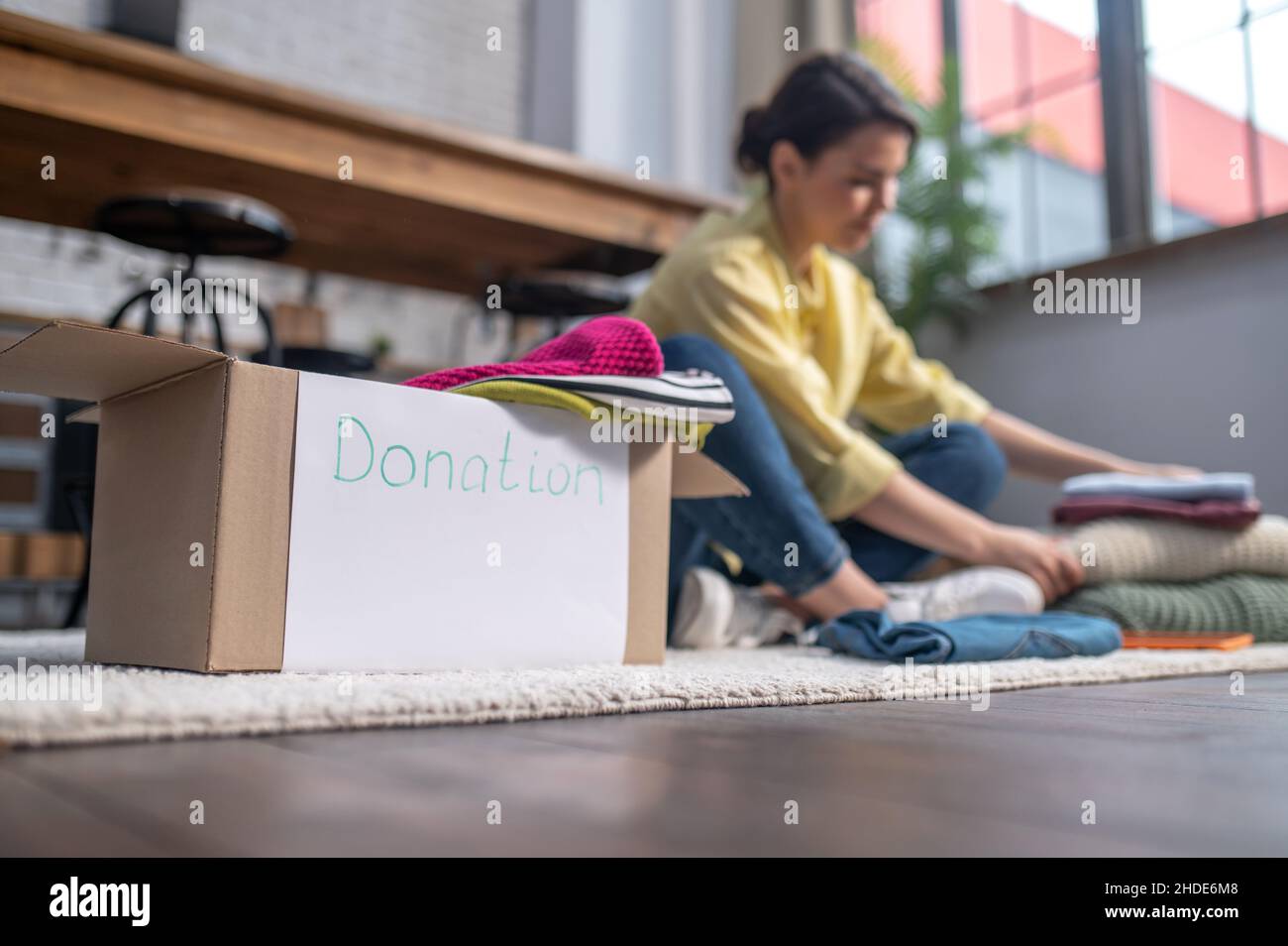 Donna seduta sul tappeto scelta dei vestiti per le cause caritative Foto Stock