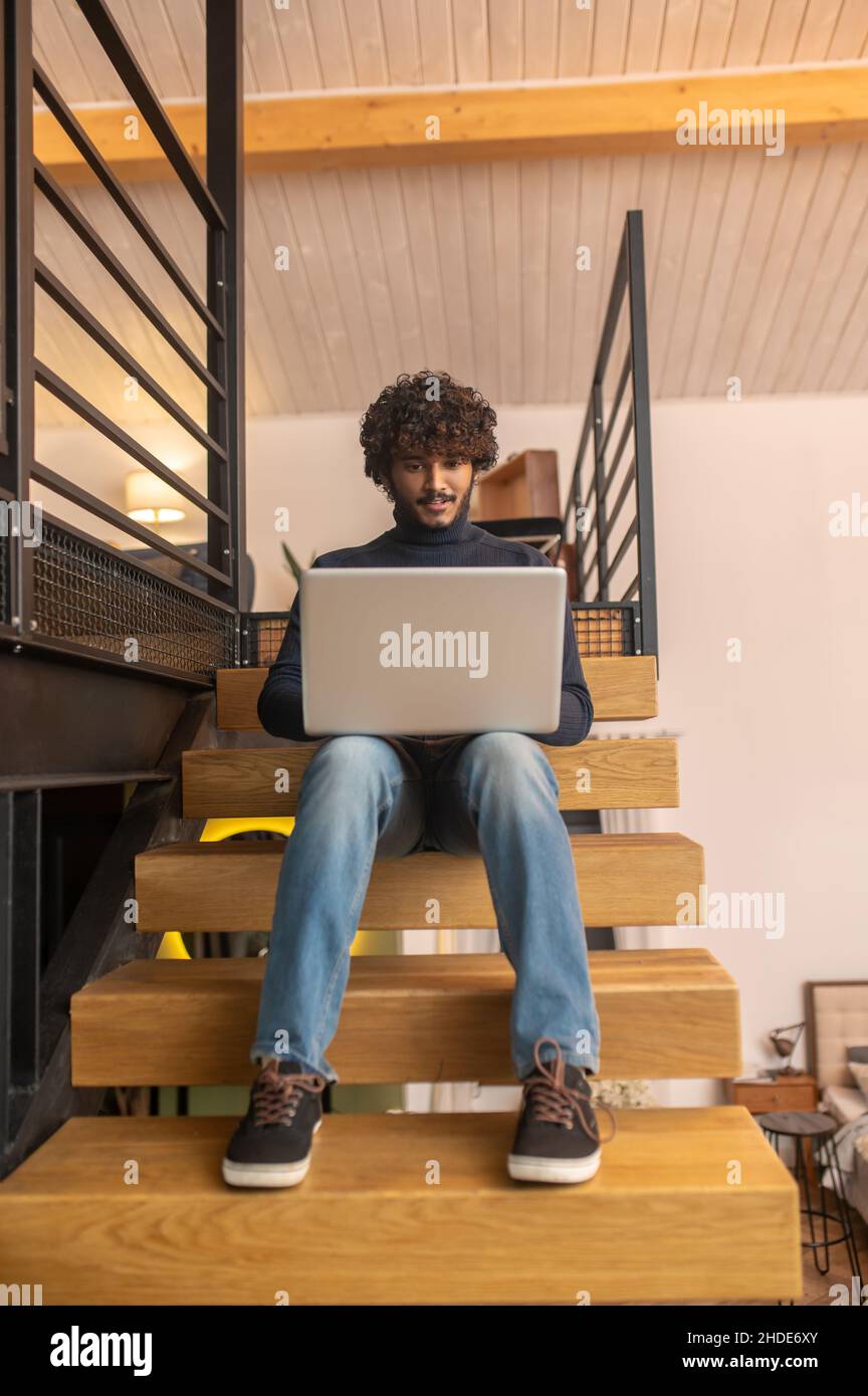 Uomo a basso angolo seduto sui gradini che lavora sul laptop Foto Stock