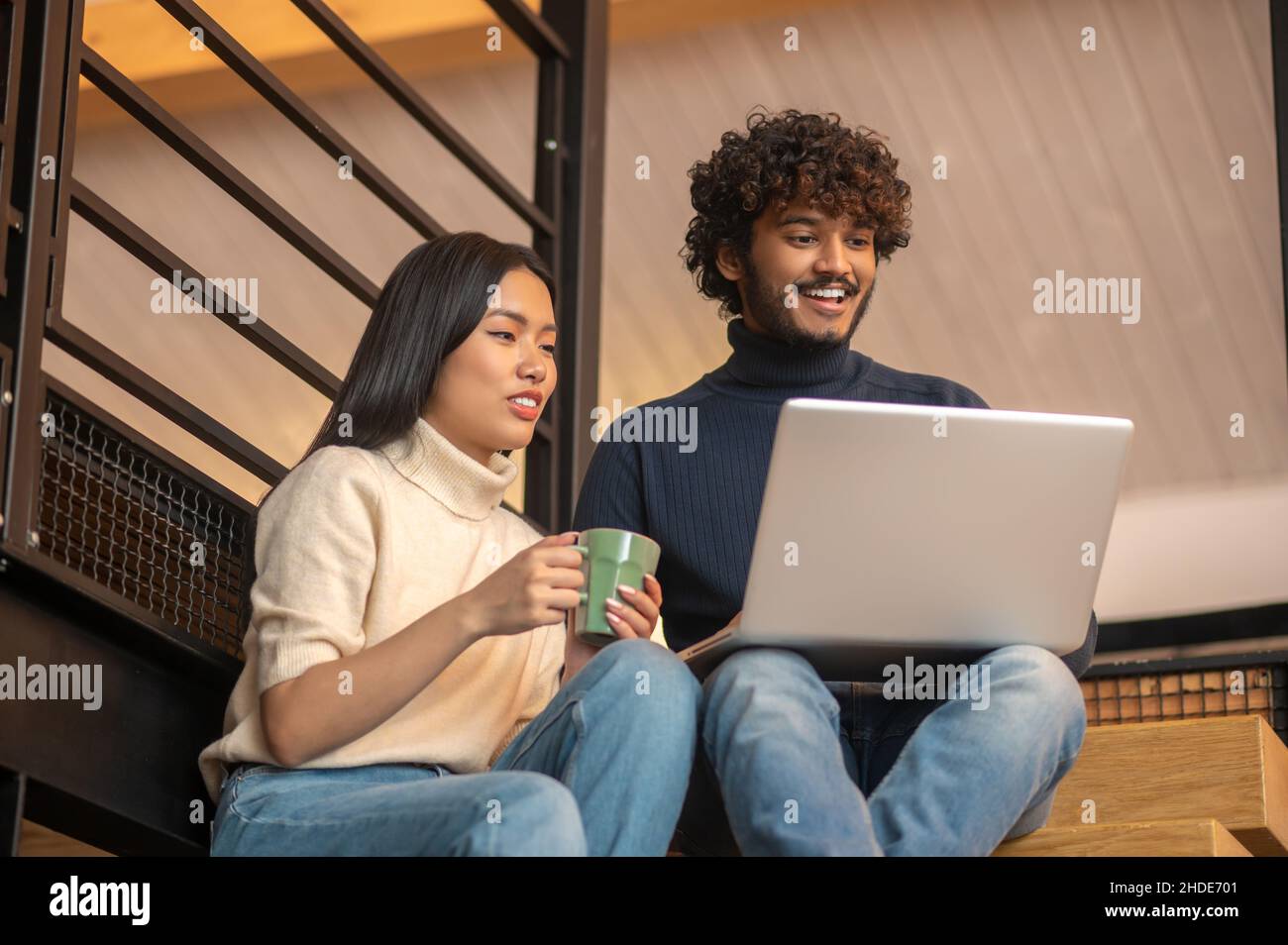 Donna con tazza e uomo che guarda il notebook Foto Stock