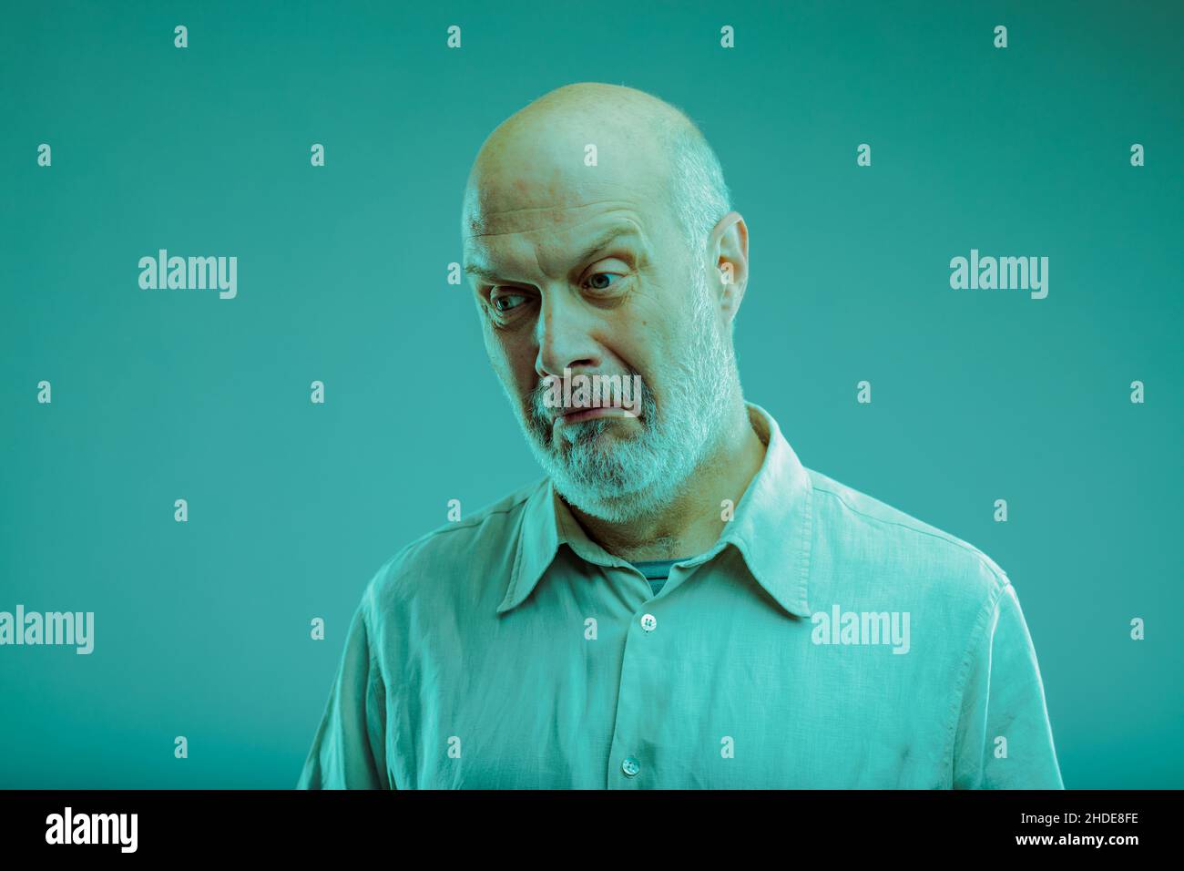 L'uomo anziano scettico che tira un volto incredulo mentre guarda lateralmente con un'espressione dubbia su blu Foto Stock