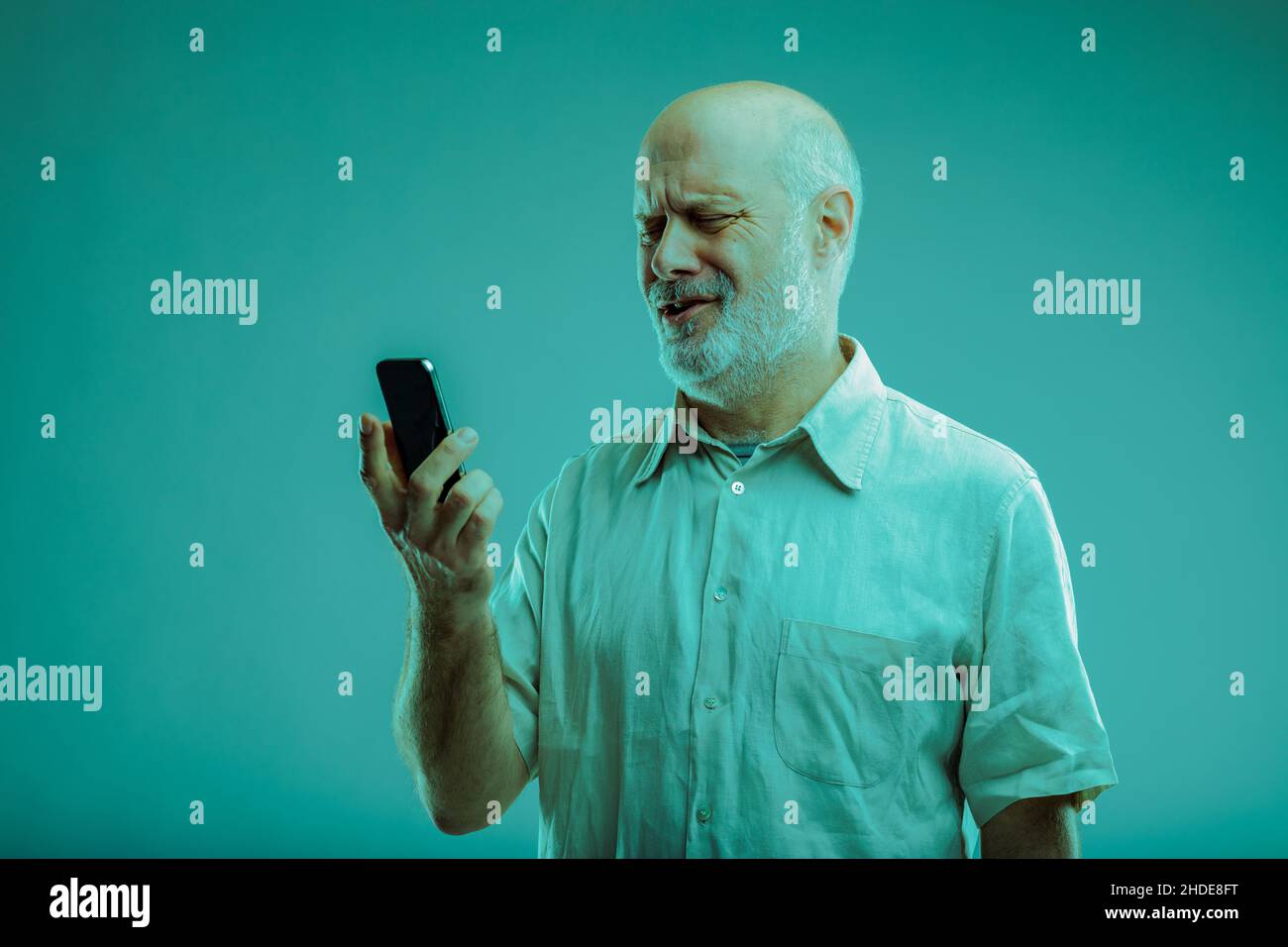 Uomo bemused che guarda il suo smartphone in confusione come lo tiene in mano per leggere un messaggio di testo o guardare i media Foto Stock