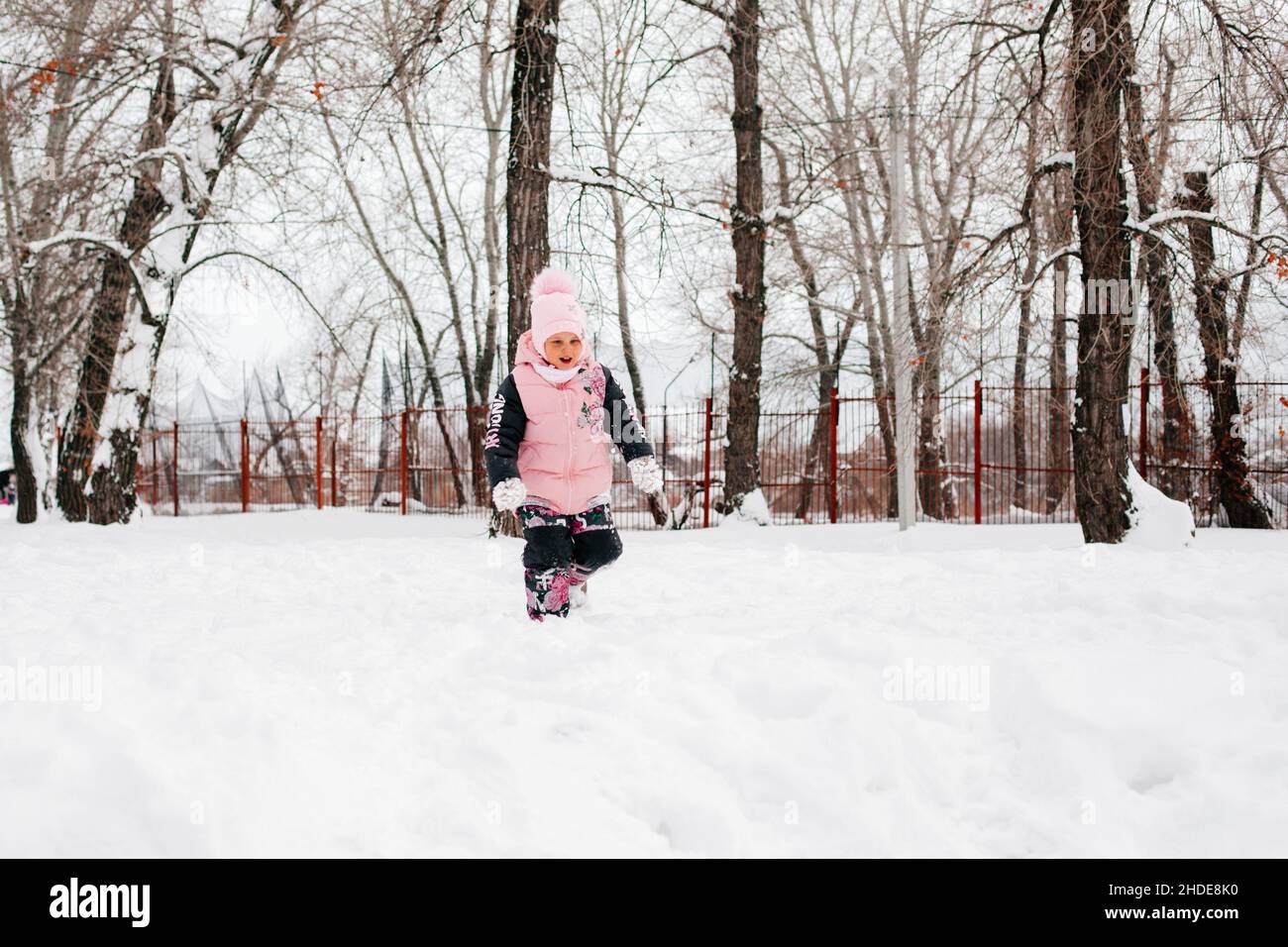 bambini che camminano nella neve e sorridono indossando abiti invernali rosa nel parco. Sfondo sorprendente pieno di bianco e neve Foto Stock