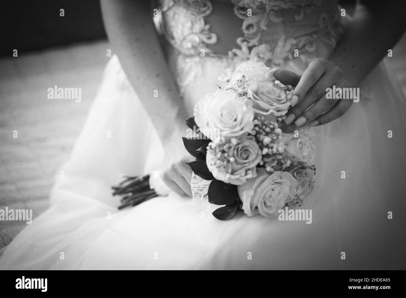 Sposa indossando un abito da sposa che tiene il suo bel bouquet in scala di grigi Foto Stock