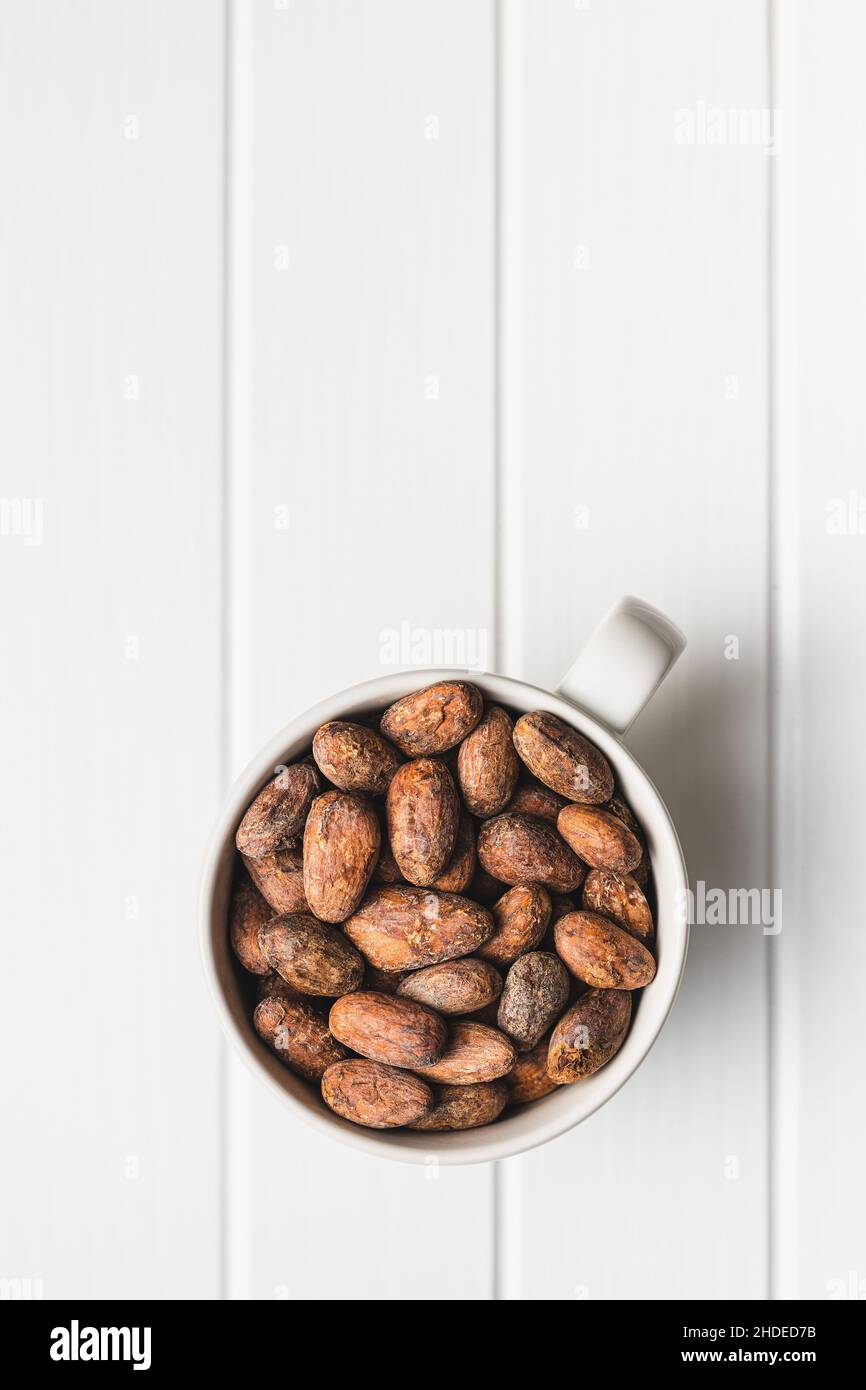 Fagioli di cacao secchi. Cacao in tazza su tavola bianca. Foto Stock