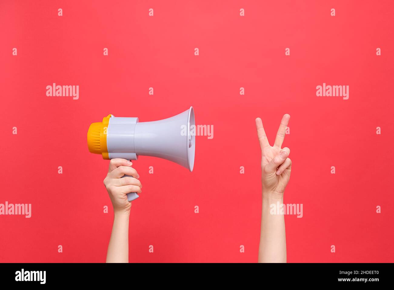 Il megaphone di tenuta della mano femminile fa il segno di pace tiene due dita in su mostra lo spazio di copia di gesto di benvenuto per il vostro soddisfare di pubblicità, isolato sul backgr rosso Foto Stock