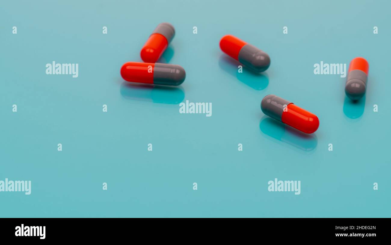 Pillola antibiotica grigia-arancione sparsa su sfondo blu. Banner farmacia. Farmaco da prescrizione. Resistenza agli antibiotici. Farmaceutico Foto Stock