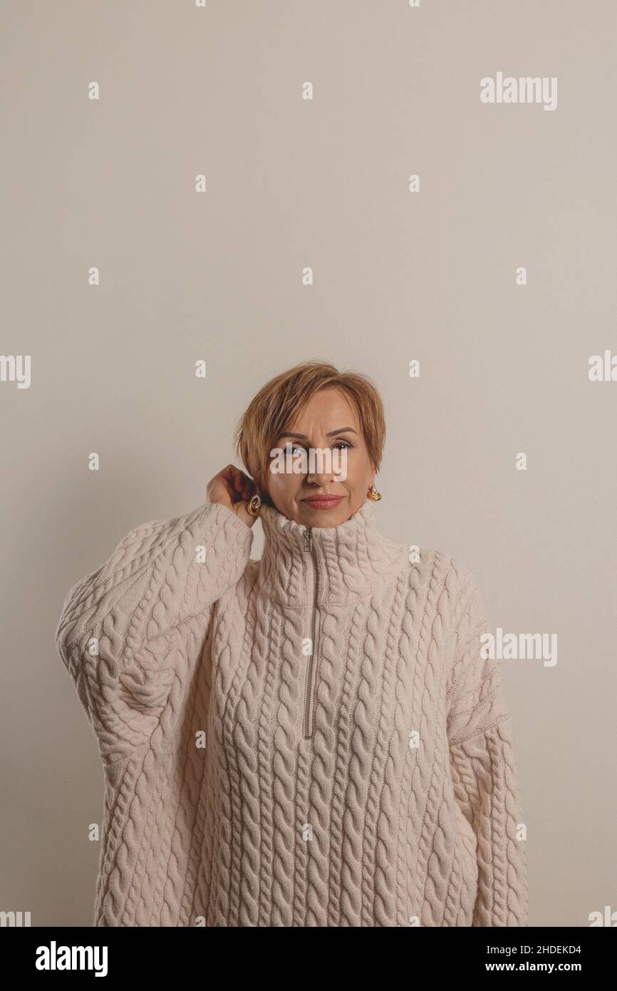 Bella donna boomer di mezza età in maglione beige su sfondo neutro. Foto Stock