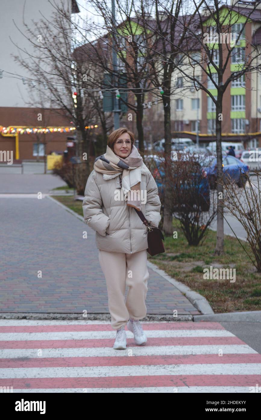 Bella donna boomer bambino di mezza età in abiti eleganti casual attraversa la strada. Foto Stock