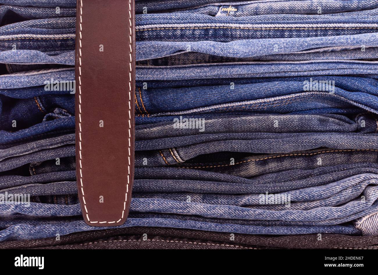 Primo piano della cintura in pelle su una pila di pantaloni in denim disponibili in vari modelli e colori. Vista laterale Foto Stock