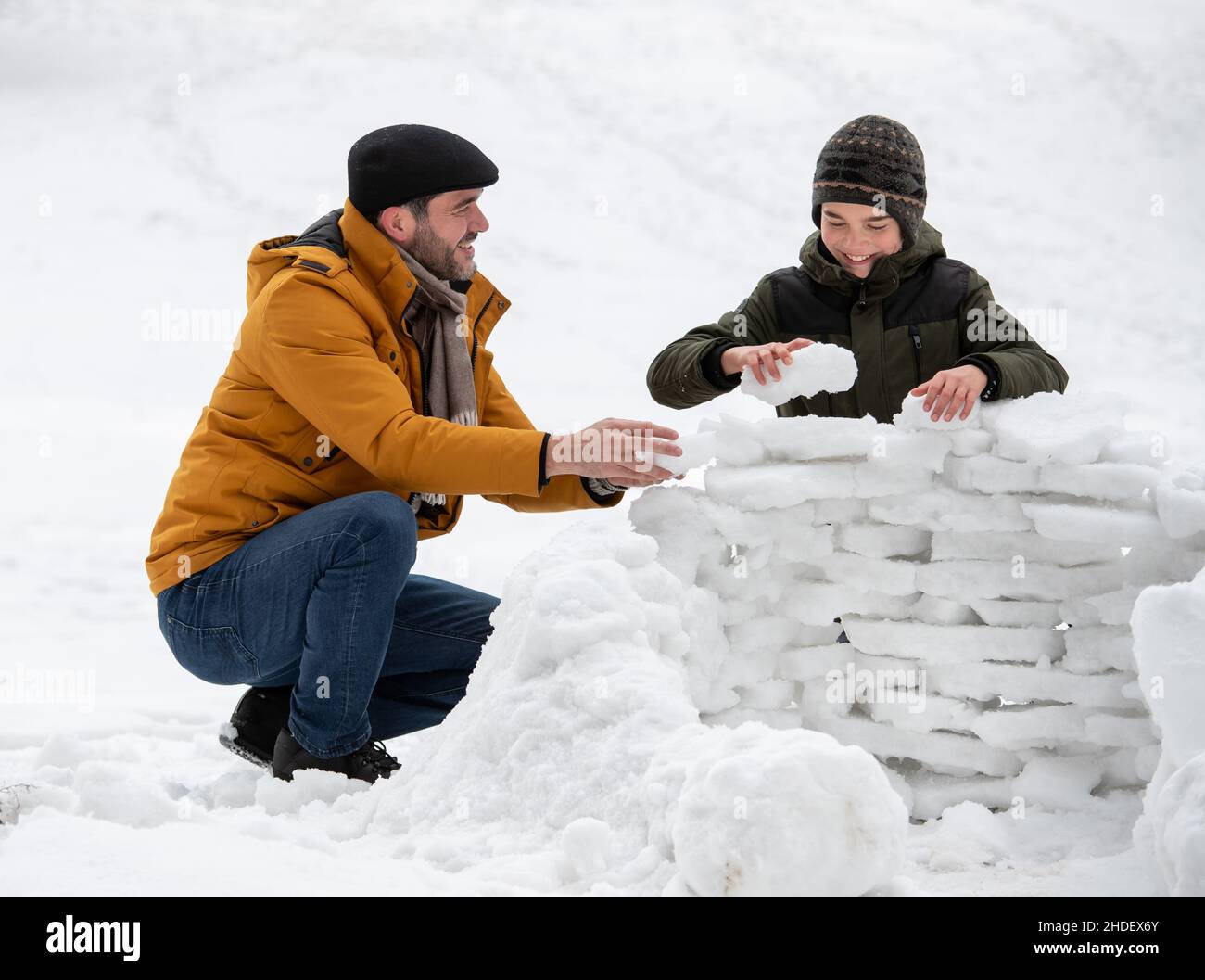 Padre e figlio giocano sulla neve, costruendo una struttura su mattoni ghiacciati di neve nel parco Foto Stock