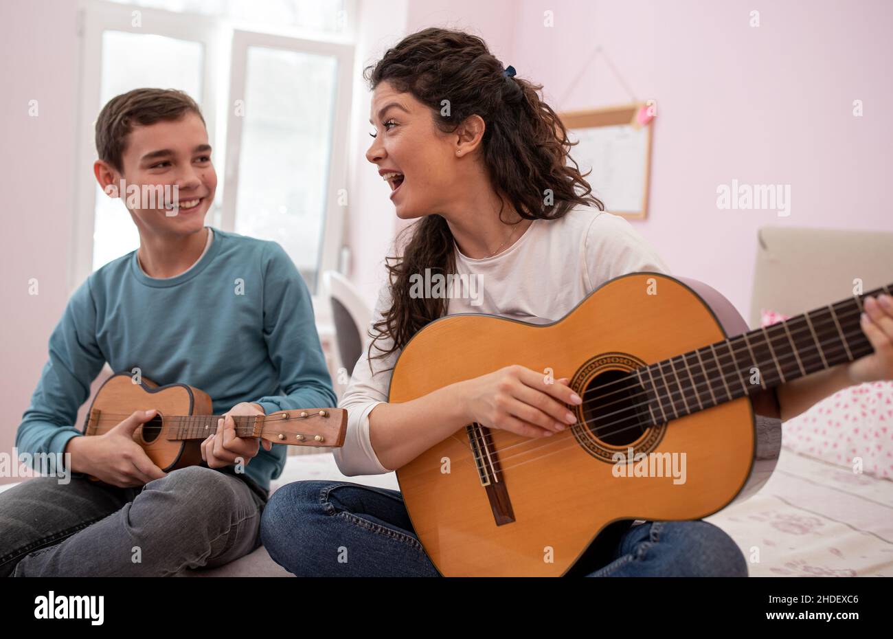 Famiglia felice, madre e figlio seduti sul letto nella stanza dei ragazzi, suonare la chitarra, cantare e divertirsi Foto Stock
