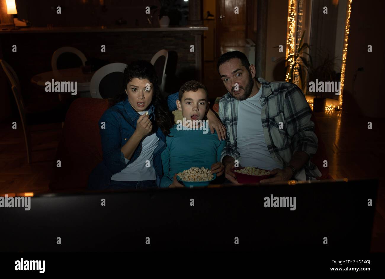 Famiglia di tre, padre, madre e figlio, guardando film horror in livingroom in buio. L'espressione del volto di Afrais e scioccata Foto Stock